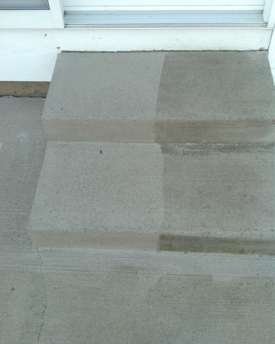 Concrete porch steps partway through pressure washing: the left half washed clean and light gray, the right half still dark and dirty