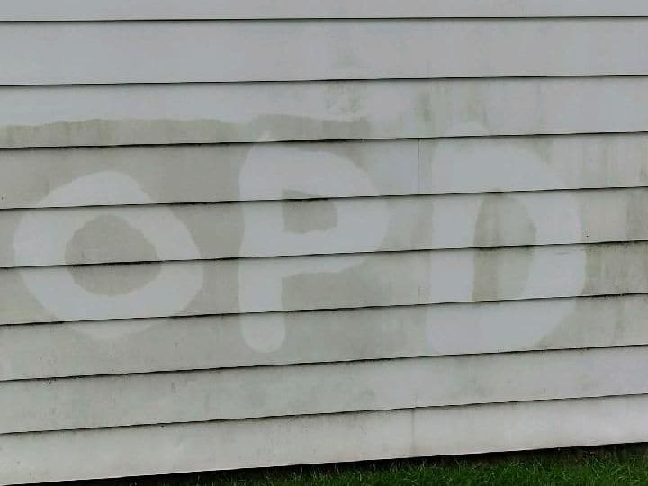 Dirty gray vinyl siding with large clean letters pressure-washed into it, showing how much grime comes off